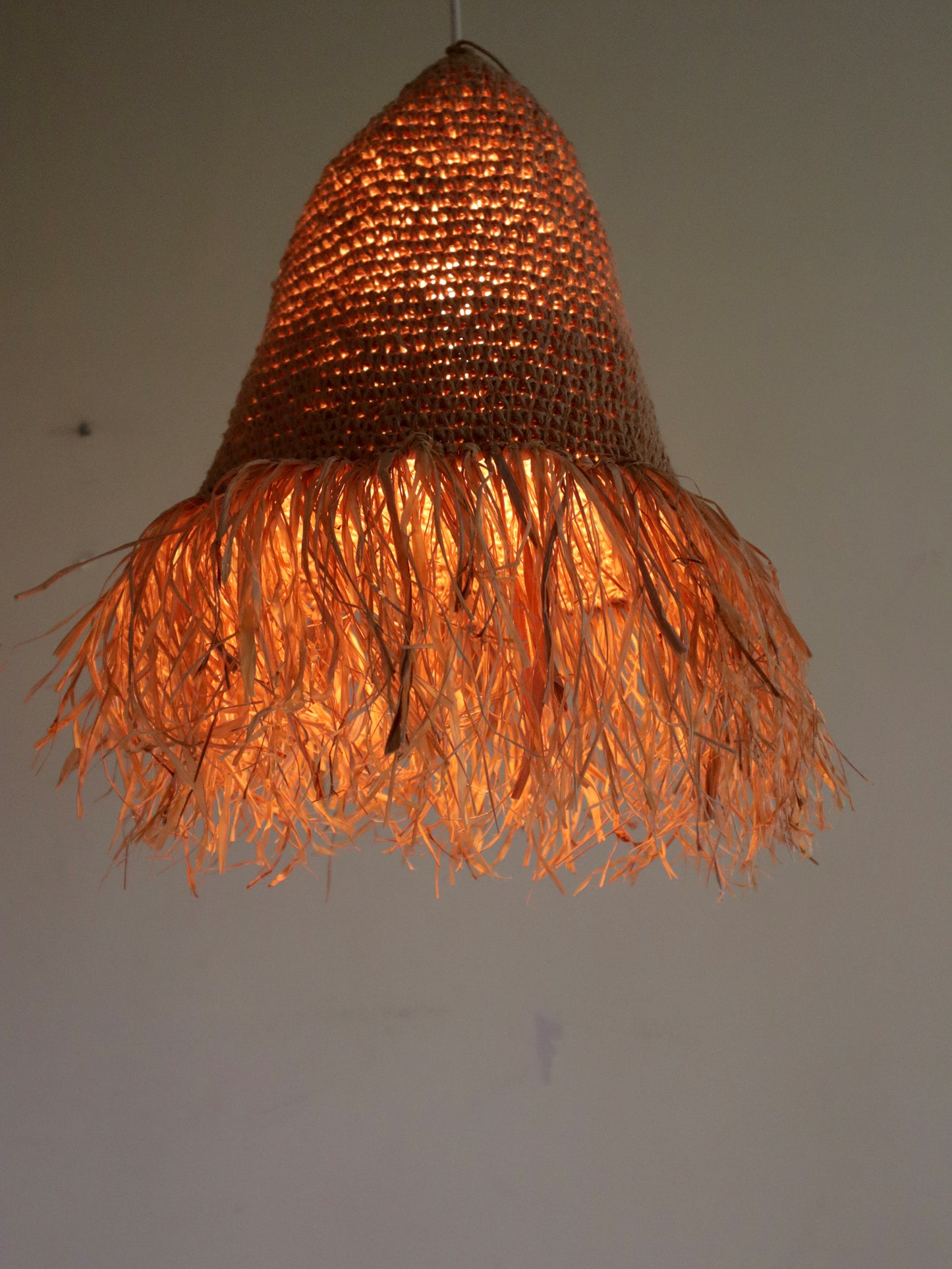 Woven pendant light with a warm glow on a plain background