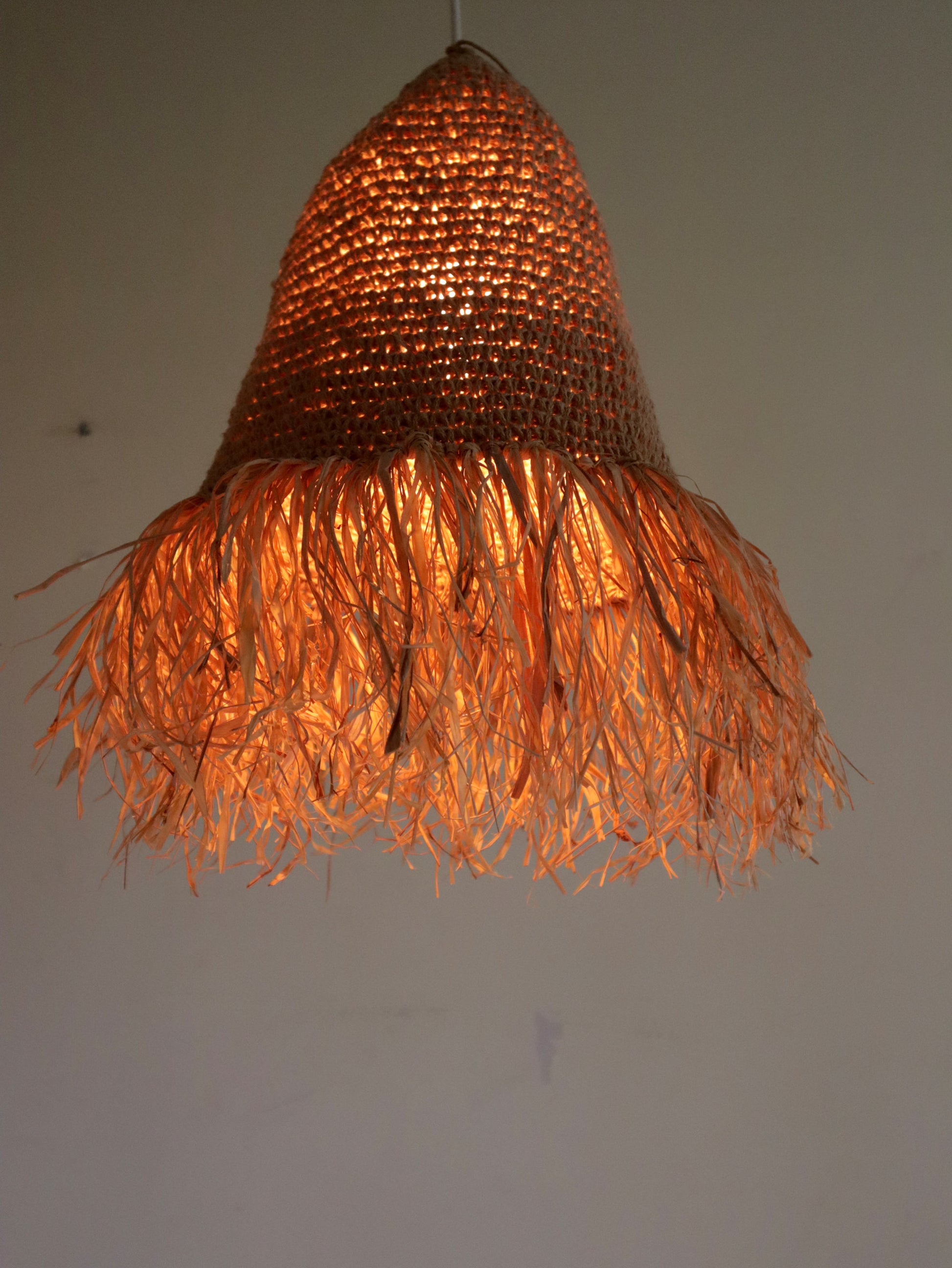 Woven pendant light with a warm glow on a plain background