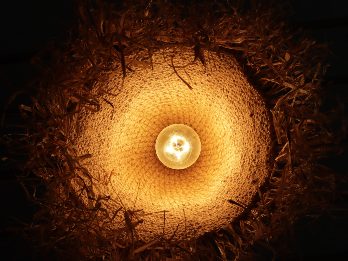 Woven Jute lampshade with a glowing light bulb inside on a dark background