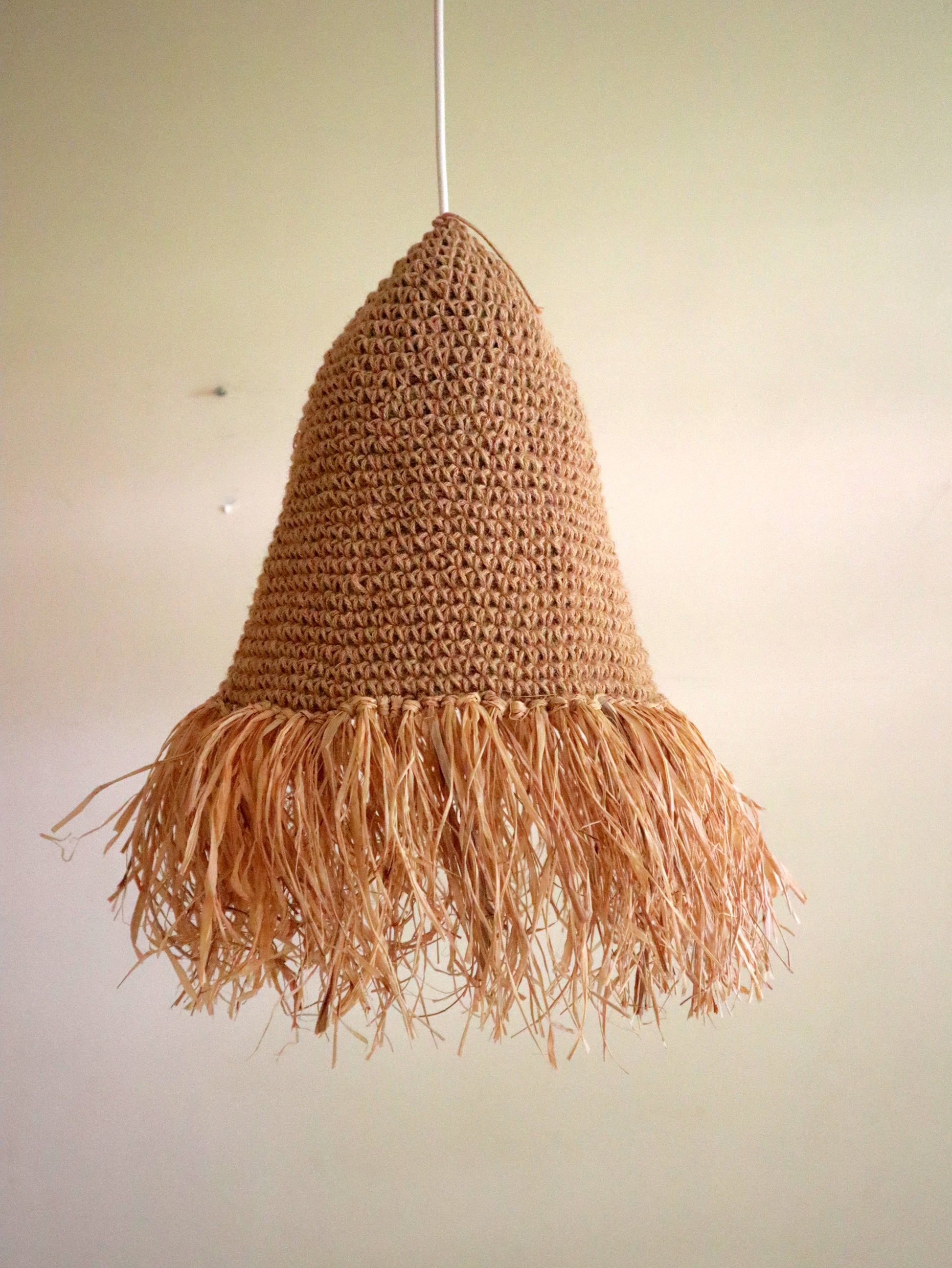 Crocheted lampshade with fringe on a plain background
