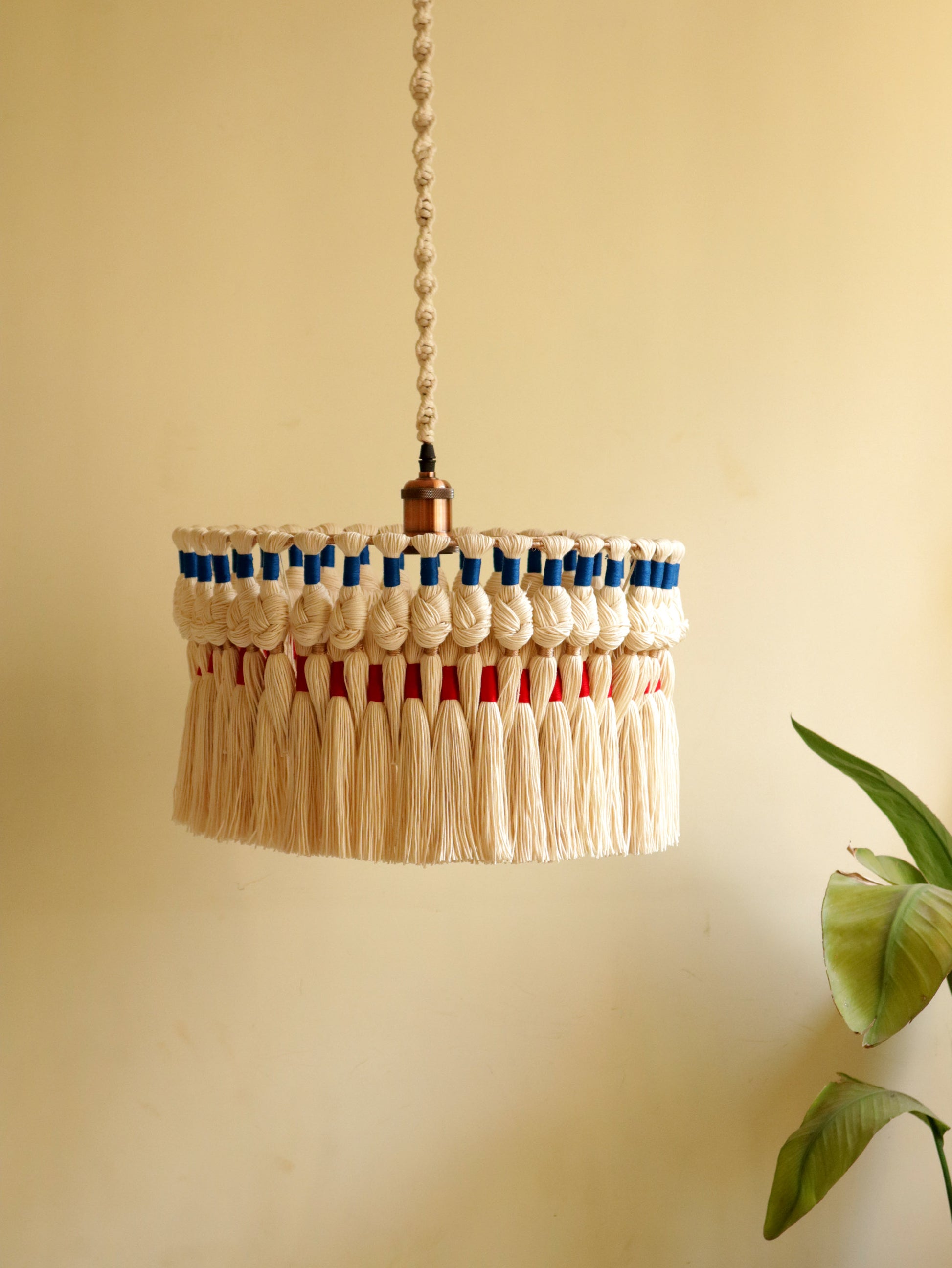Handwoven macrame pendant light with natural cotton cords, red and blue woven accents, and long fringe — boho ceiling lampshade handmade by The Woven Sutra.