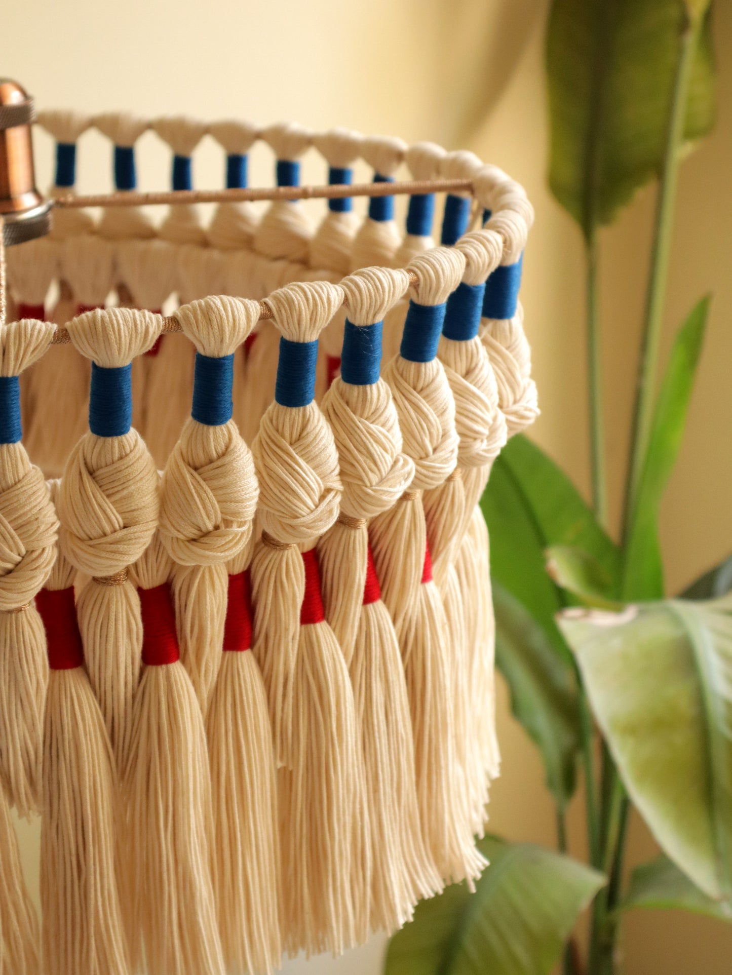 Decorative wall hanging with tassels in beige, blue, and red against a neutral background.