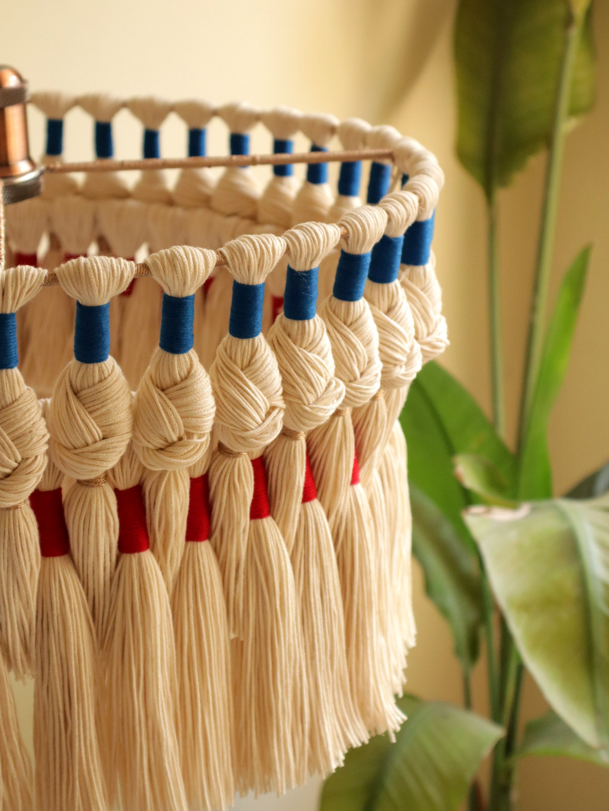 Decorative wall hanging with tassels in beige, blue, and red against a neutral background.