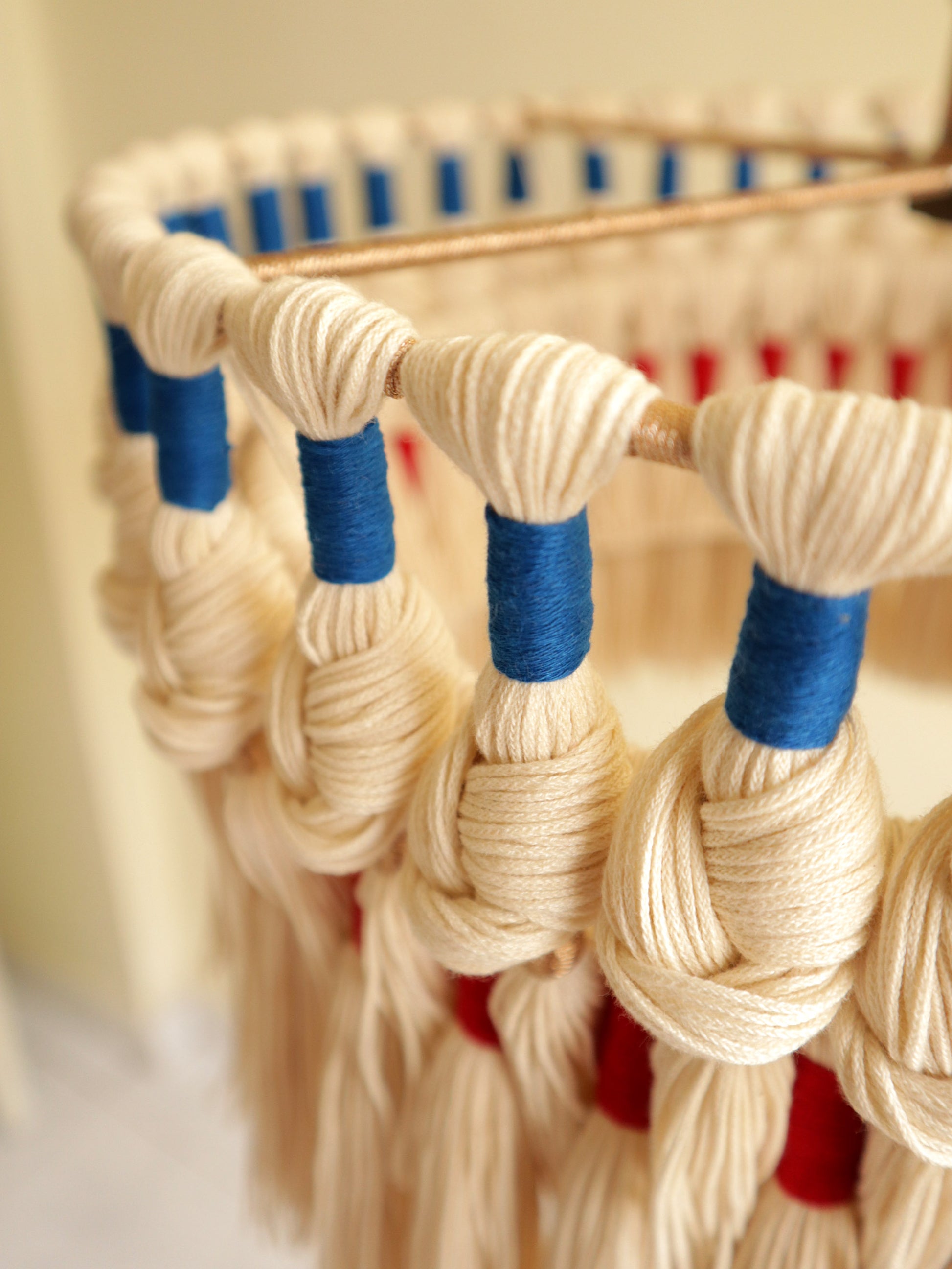 Close-up of macrame knots and colorful woven details in natural, red, and blue cotton cords on a handmade boho hanging lamp.