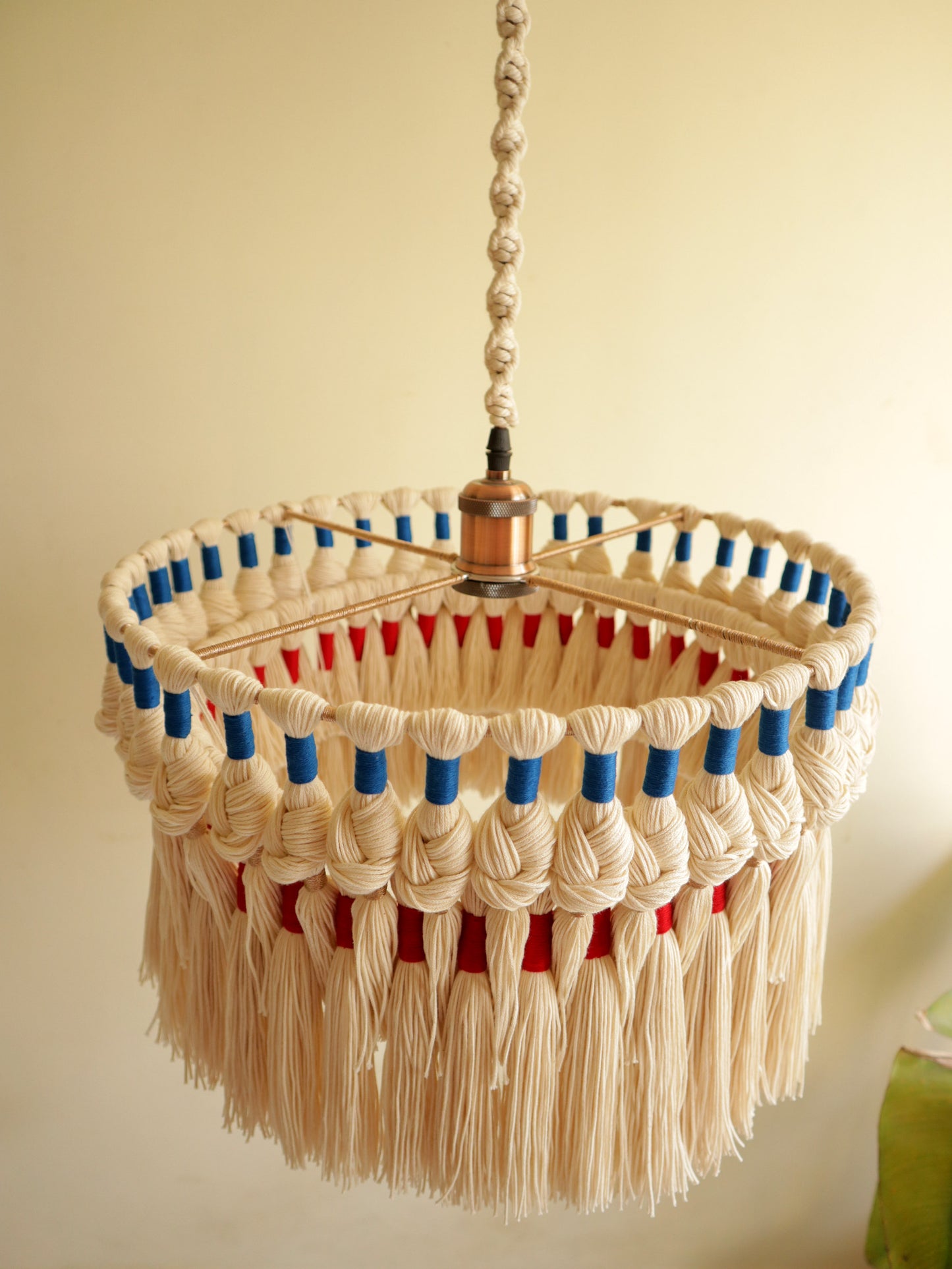 Side view of a handcrafted macrame ceiling light with layered tassel fringe and woven pattern — sustainable cotton lighting design.